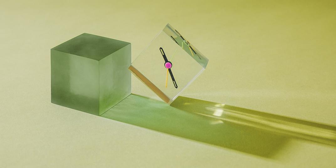 Two glass cubes rest on a green surface, one with a clock on its front surface.
